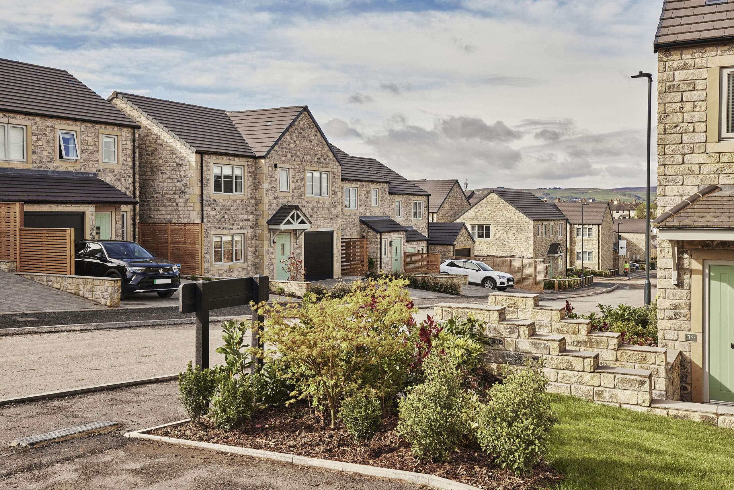 Natural stone homes with green front doors along a gently curving street at The Alders, Skipton